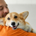 A vet wearing orange scrubs holds a Corgi as he shares vet advice on understance pet cancer