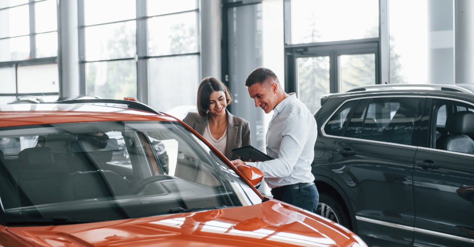 A man and woman examine a car in a showroom, discussing options related to car insurance
